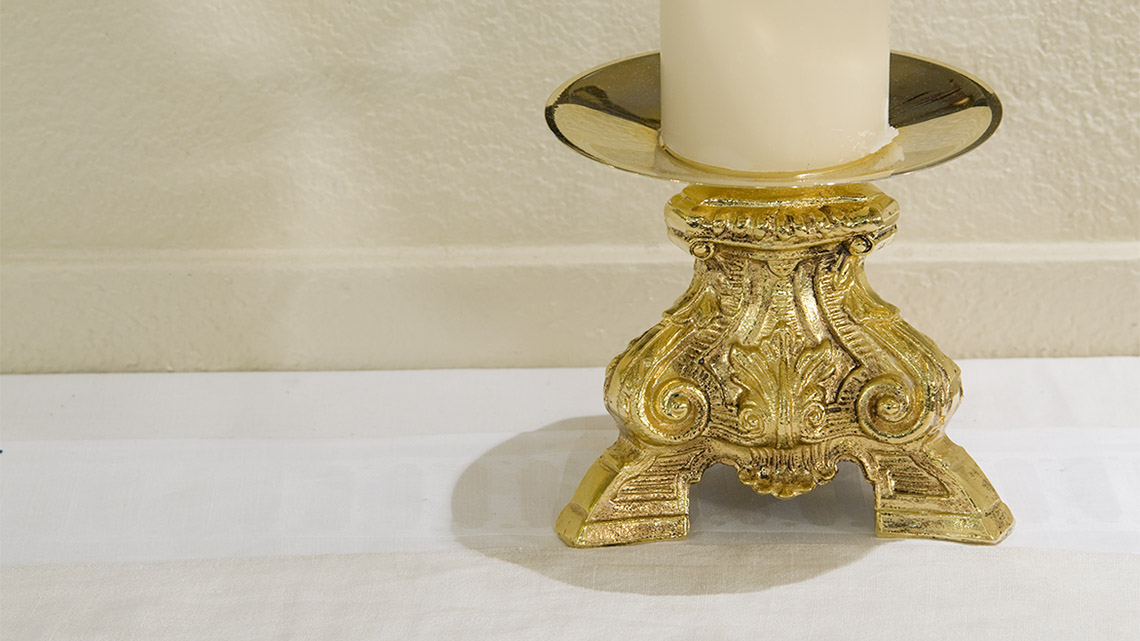 Photo of brass candlestick on white altar. 